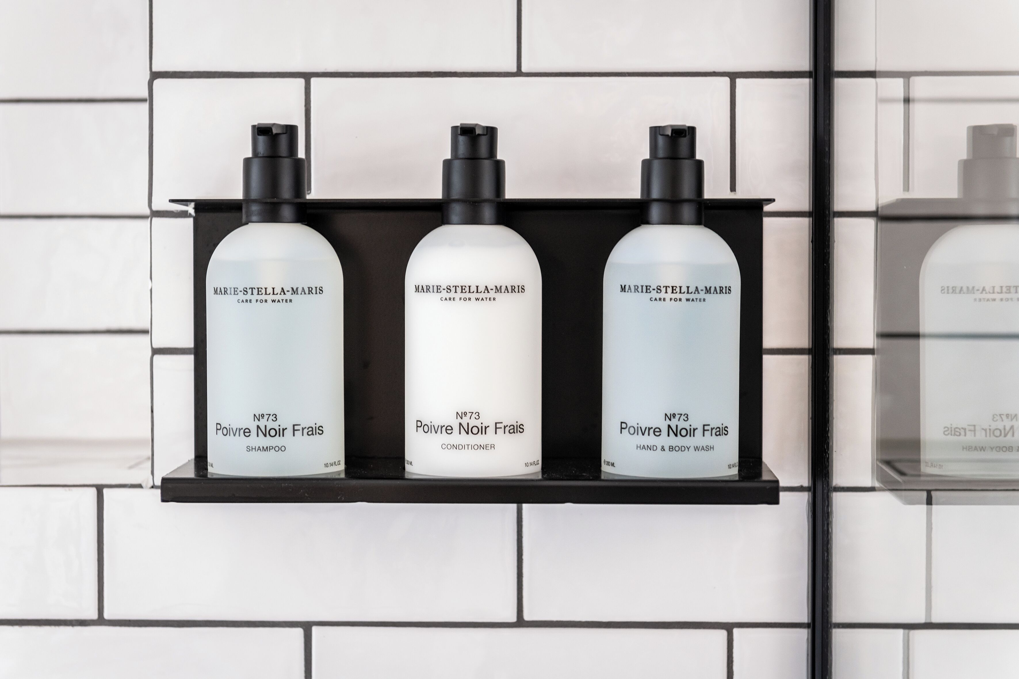 Trois bouteilles de produits Marie-Stella-Maris sont posées sur une étagère noire, devant un mur recouvert de carreaux blancs.