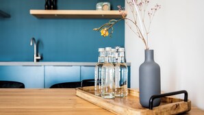 Een houten tafel met een dienblad waarop heldere flessen en een grijze vaas met gedroogde bloemen staan.