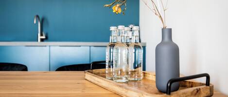 A wooden table with a tray holding clear bottles and a gray vase with dried flowers.