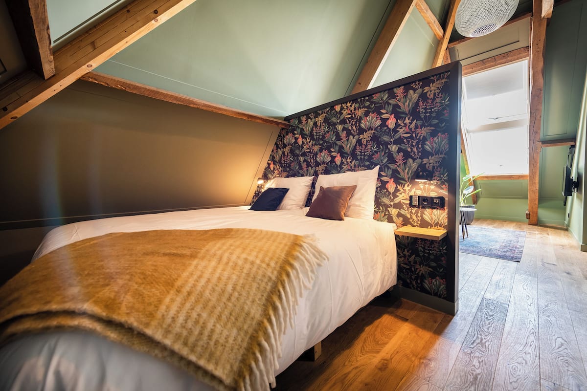 Un dormitorio con techo de madera, una cama con cabecera estampada y vistas al cielo a través de un tragaluz.
