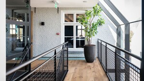Een modern interieur met een houten vloer, metalen balustrade, een grote potplant en een witte baksteenmuur.