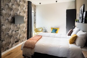 Una habitación de hotel con cama, televisor montado en la pared, puerta y ventana con cortinas.
