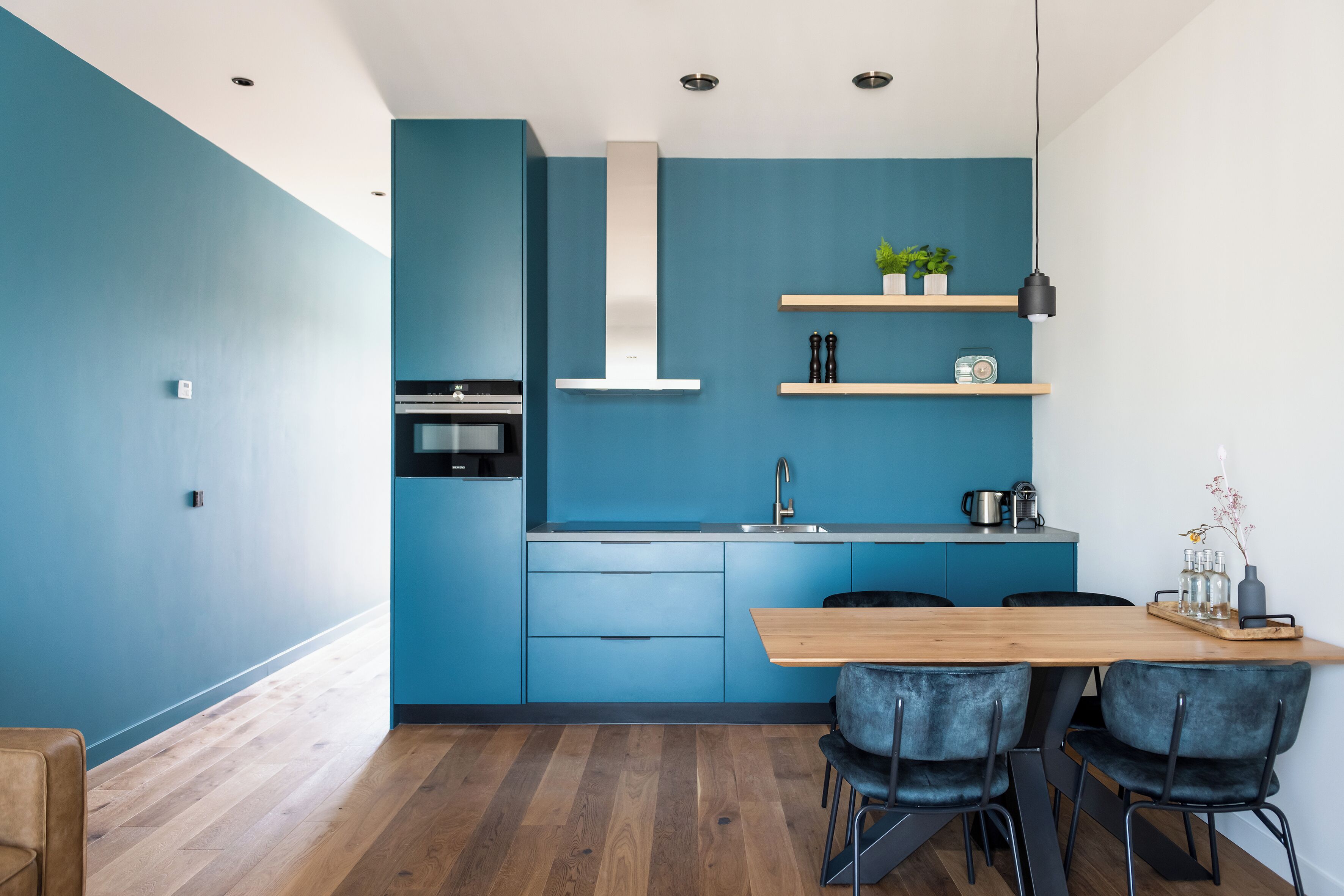 A modern kitchen with blue cabinetry, a wooden dining table, and black chairs.
