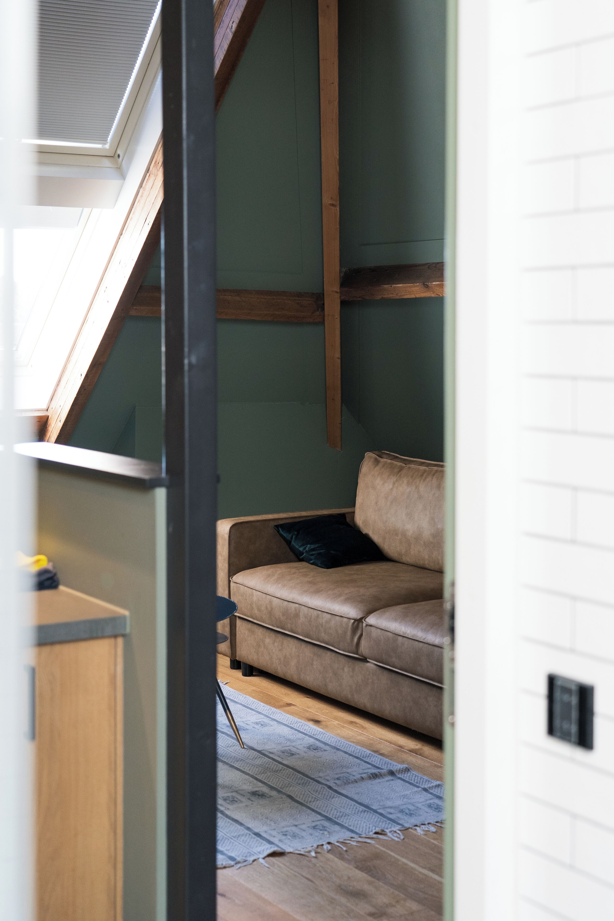 Une pièce avec un canapé en cuir marron, un plancher en bois et une lucarne.