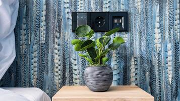 Una cama bien hecha con ropa de cama blanca, una mesita de noche con una planta en maceta y una lámpara de pared.