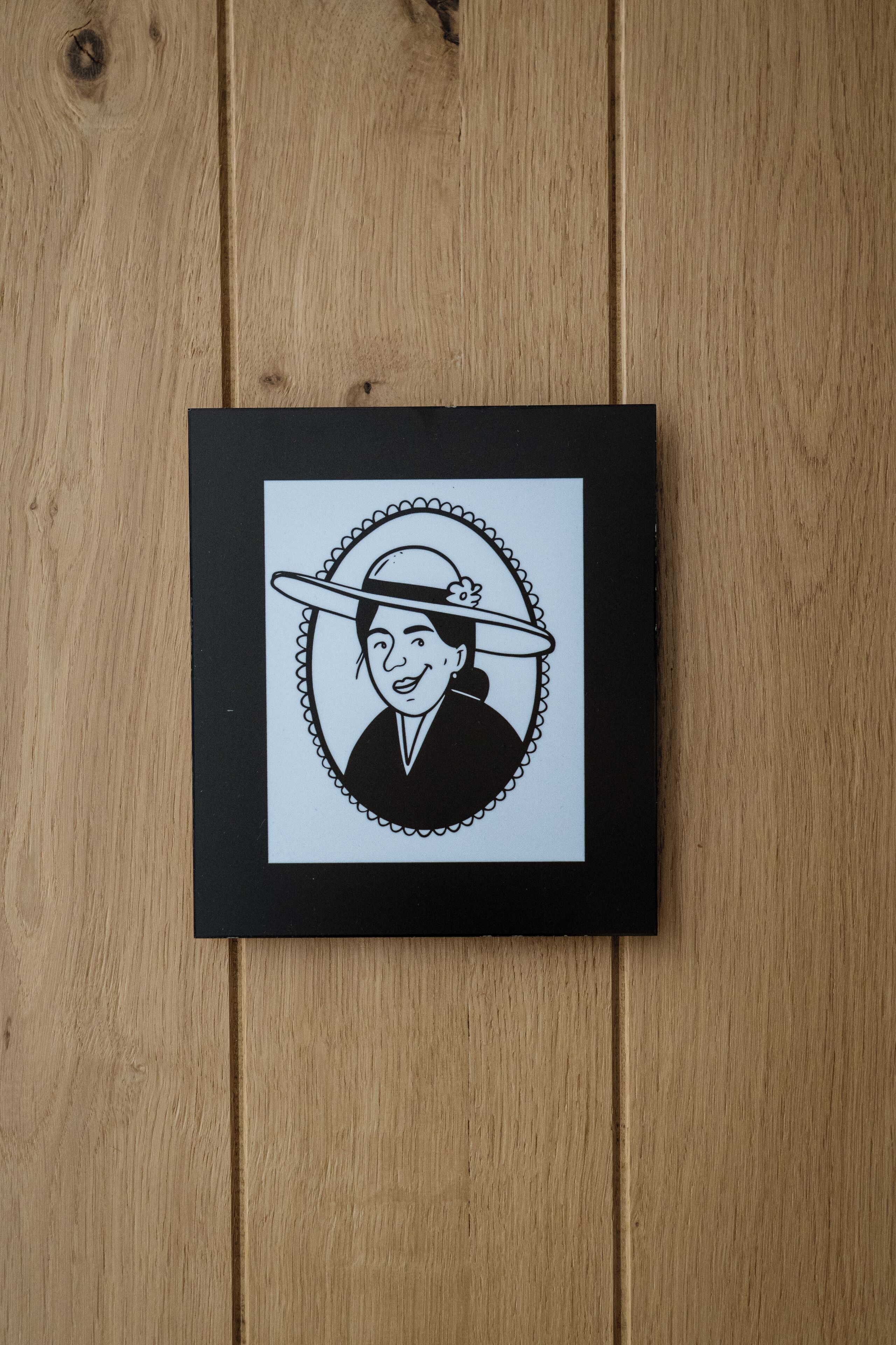 A framed black and white illustration of a person wearing a hat on a wooden surface.