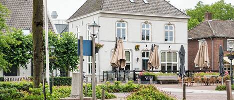 Un bâtiment traditionnel avec un toit en tuiles, une entrée centrale et un espace extérieur aménagé avec des tables et des parasols.