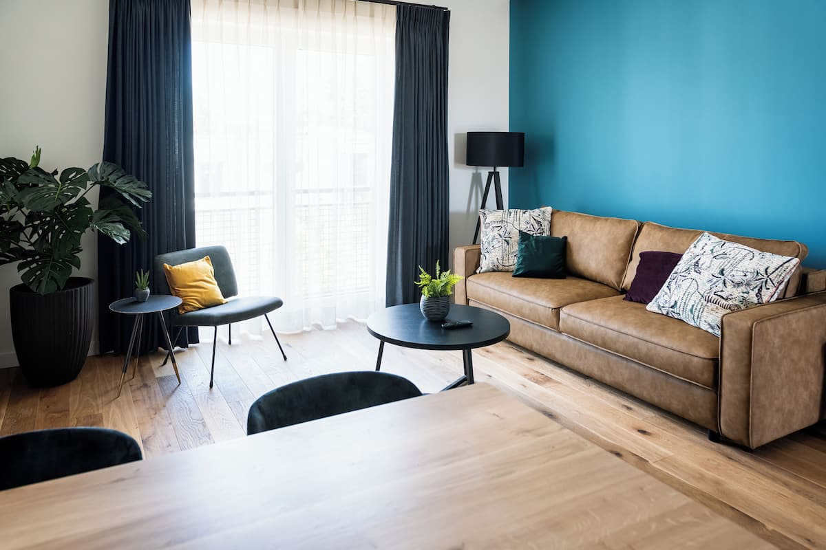 Una sala de estar moderna con un sofá marrón, una mesita de centro redonda, una silla negra y una planta grande en maceta.