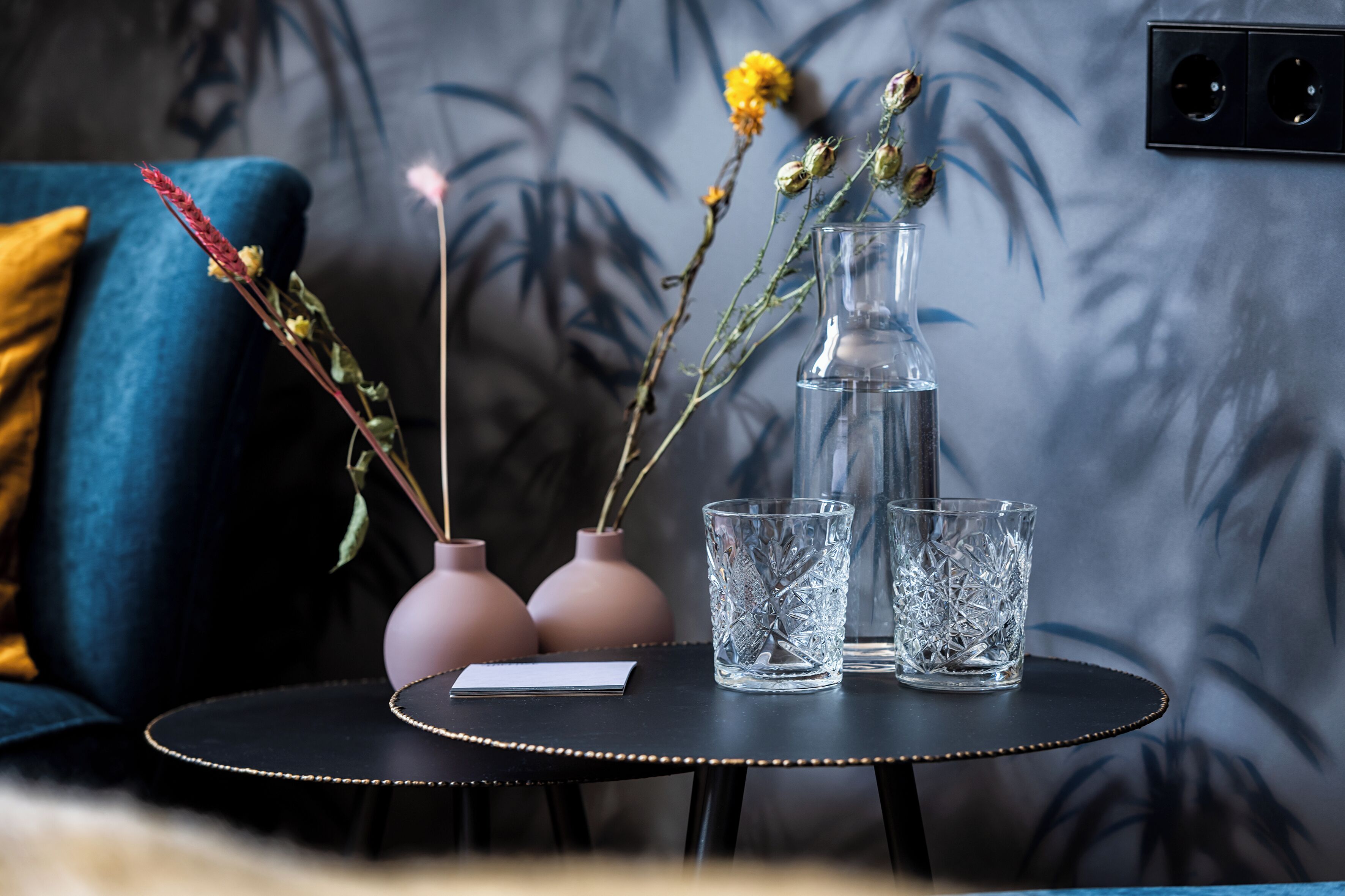 A small round table with two pink vases, a clear glass pitcher, and two clear glass cups.