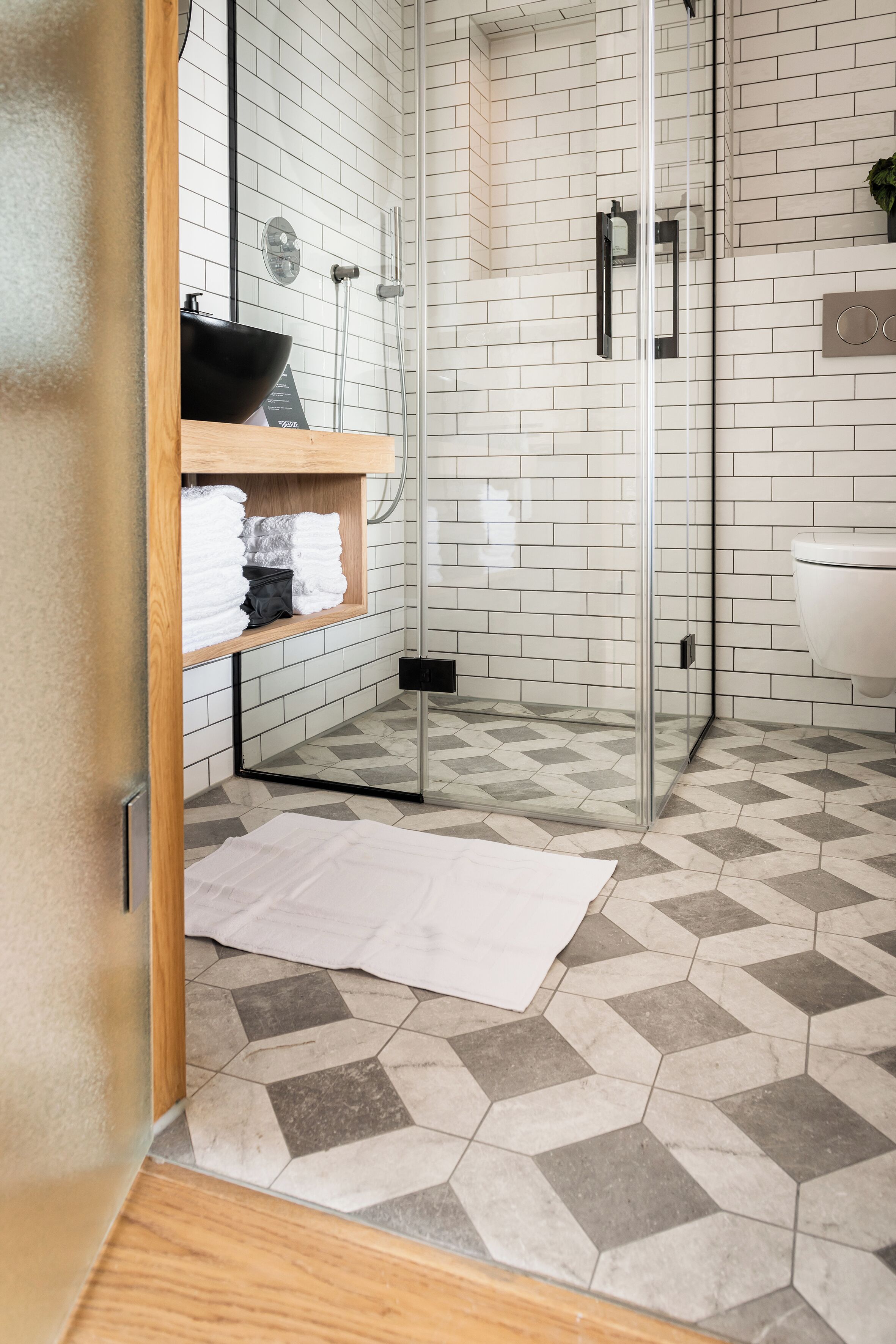 Un baño moderno con cabina de ducha de vidrio, un lavabo negro y un estante de madera con toallas.