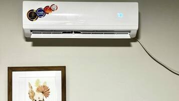 Un climatiseur mural doté d’un écran numérique, d’un câble d’alimentation et d’un cadre contenant une image de fleurs placé en dessous.