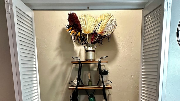 Un estante de madera de varios niveles con objetos decorativos, frente a una pared lisa con una puerta a cada lado.
