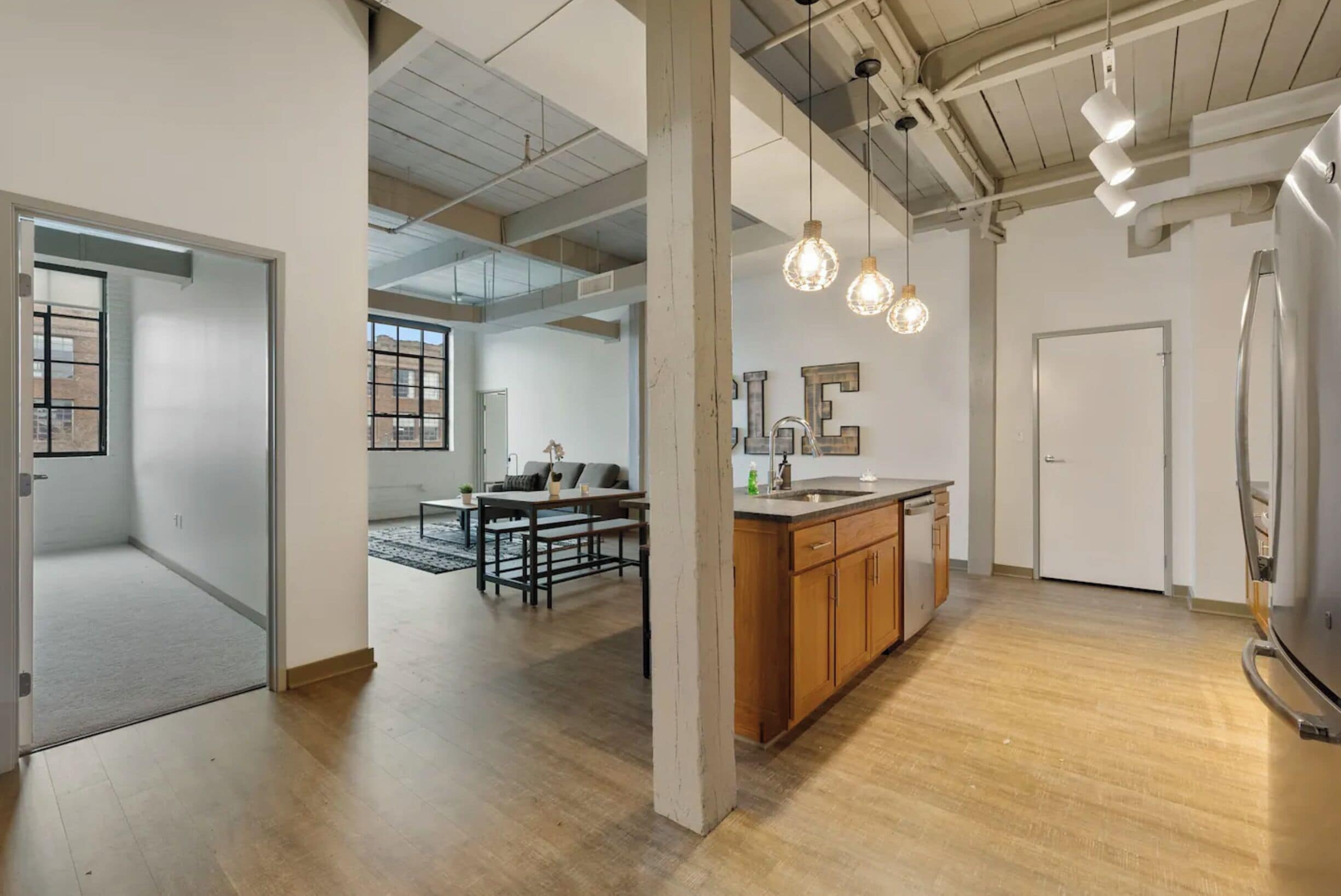 A spacious open-plan living area with a kitchen, wooden flooring, and exposed ceiling beams.