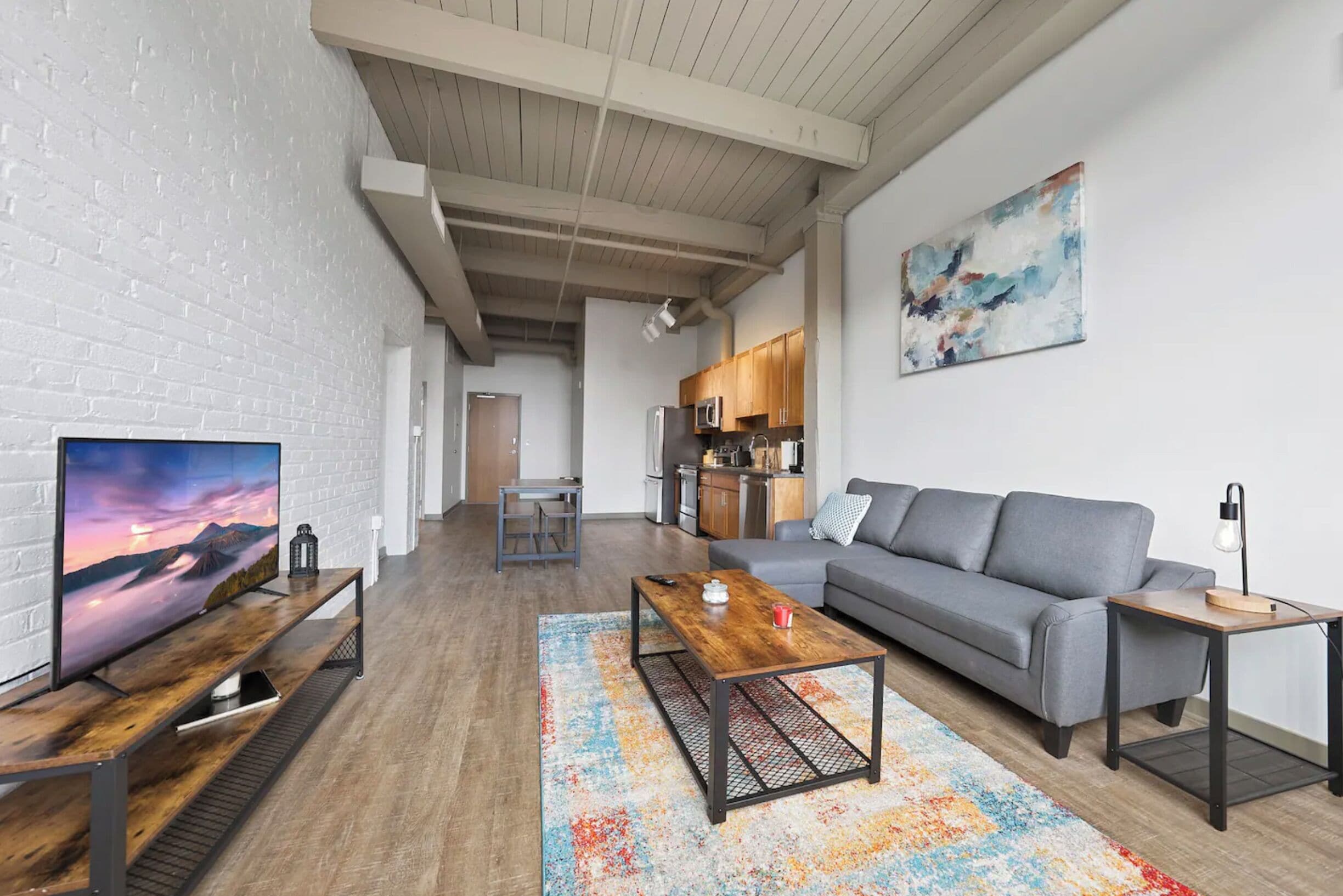 A modern living room with a grey sofa, wooden coffee table, and a TV on a wooden stand.