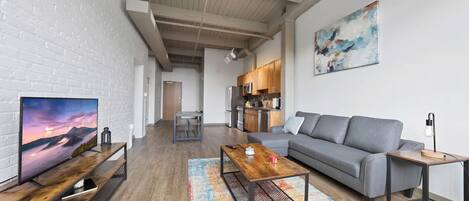 A modern living room with a grey sofa, wooden coffee table, and a TV on a wooden stand.