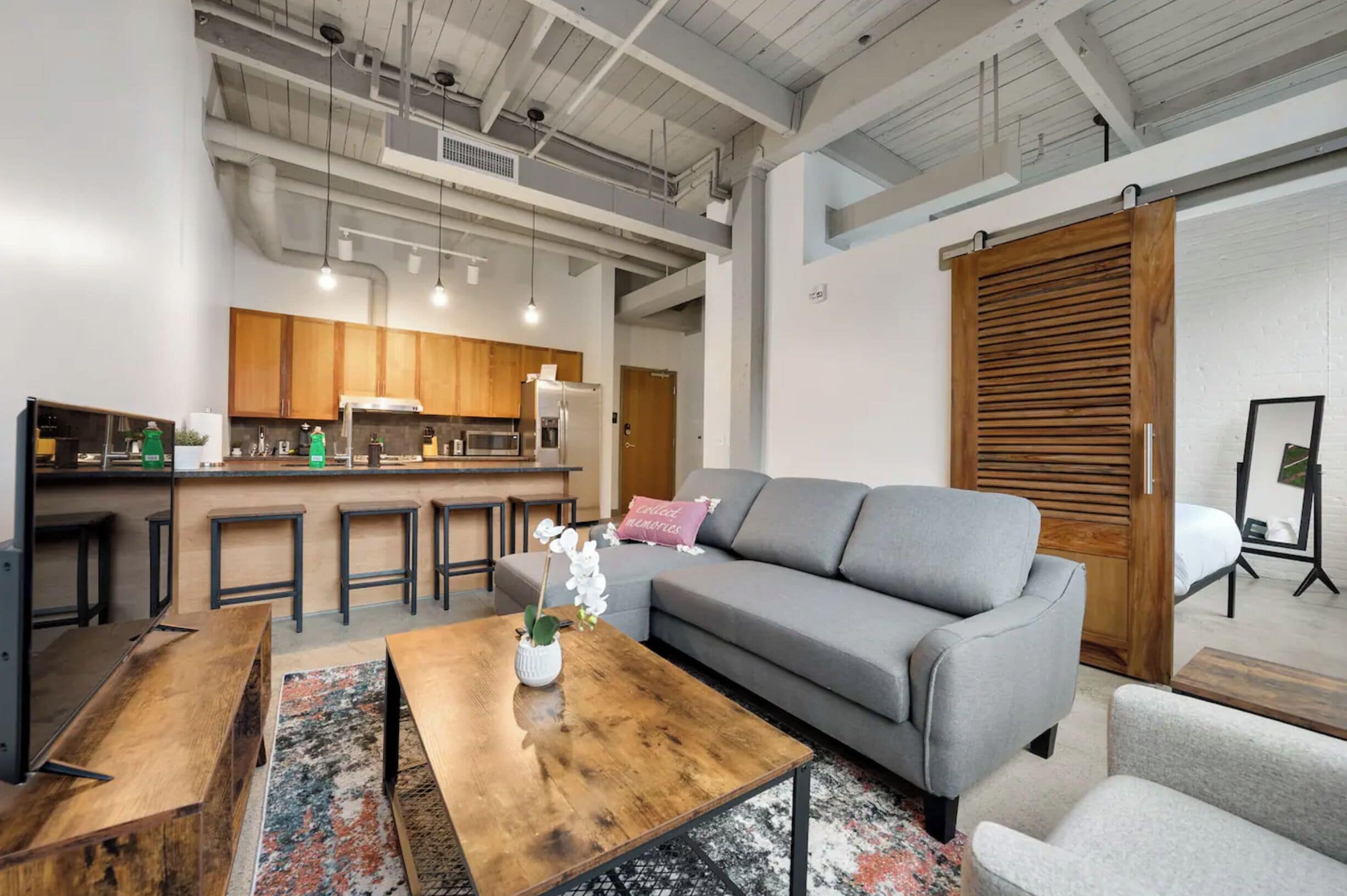 A modern interior with a kitchen area, grey sofa, wooden coffee table, and a large wooden door.