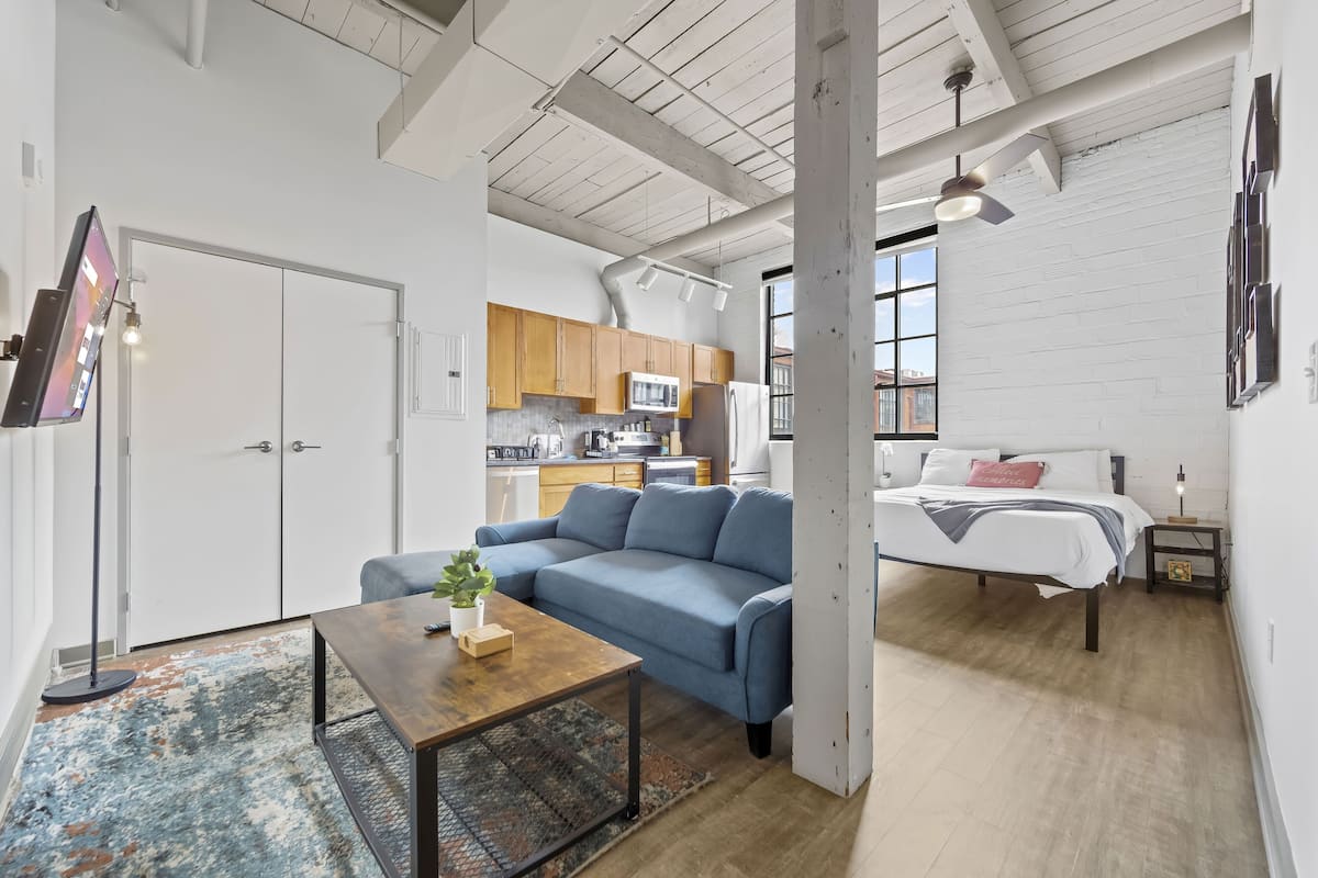 A modern living space with a sofa, a coffee table, a bed, and a kitchen area.