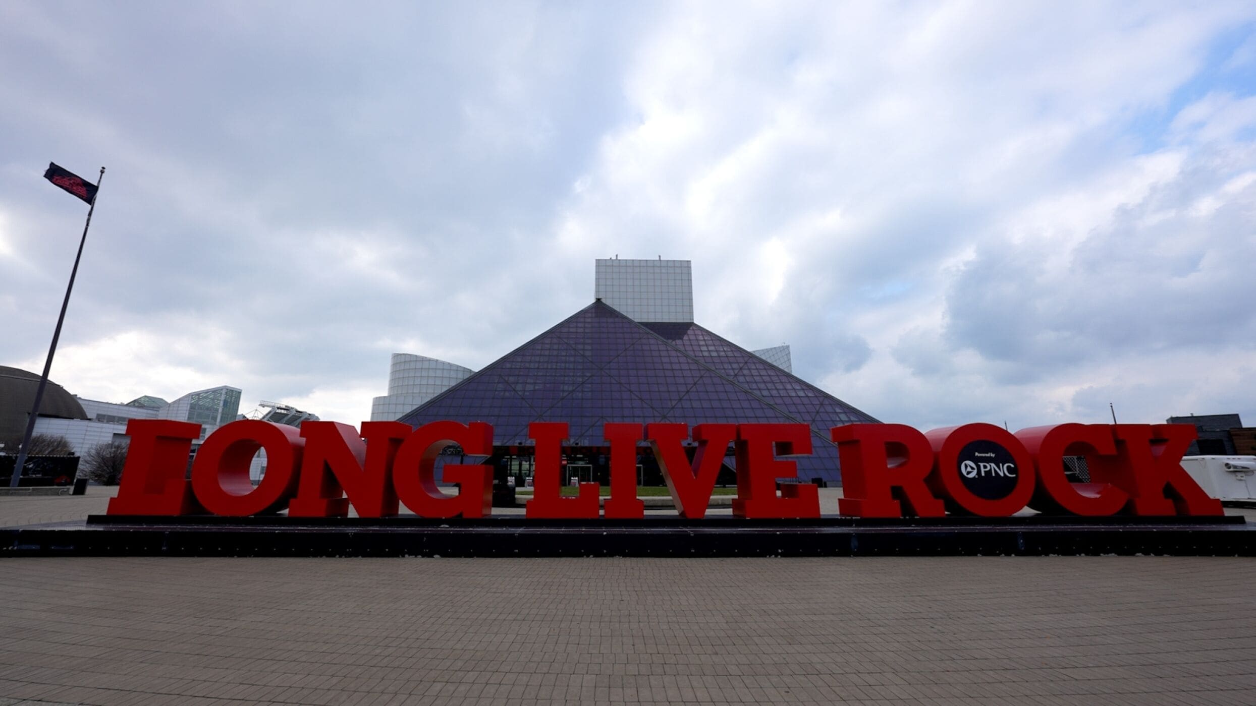 Een groot rood bord met de tekst 'Tong Live Rock' voor een modern gebouw met een glazen dak.