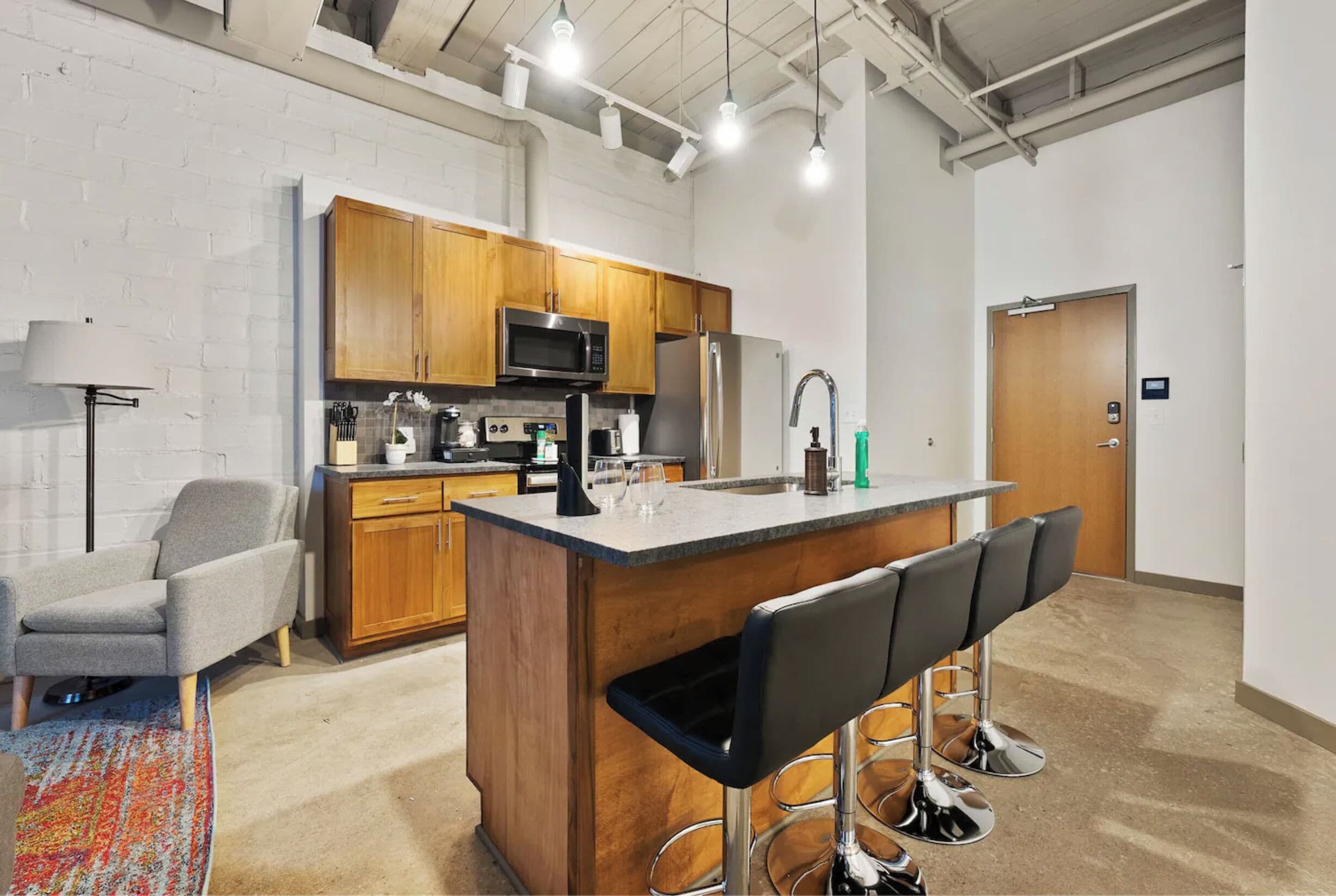 A modern kitchen with wooden cabinets, a stainless steel refrigerator, a microwave, and a bar area with stools.
