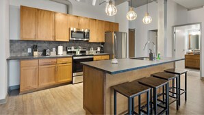A modern kitchen with wooden cabinets, stainless steel appliances, and a central island with stools. - 2125 Superior Living (Cleveland)