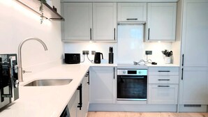 Una cocina moderna con armarios blancos, horno empotrado, lavavajillas y un lavabo con grifo.