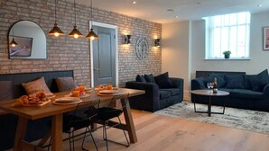 Una sala de estar moderna con pared de ladrillo, mesa de comedor de madera, sillas negras, sofá oscuro y una pequeña mesa de centro.