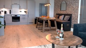 Una cocina moderna con armarios blancos, un comedor con mesa de madera y una pared de ladrillo.