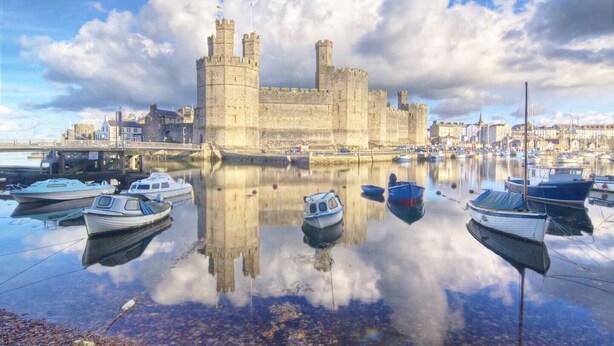 Un castillo histórico con un foso, rodeado de barcos y un paisaje urbano.