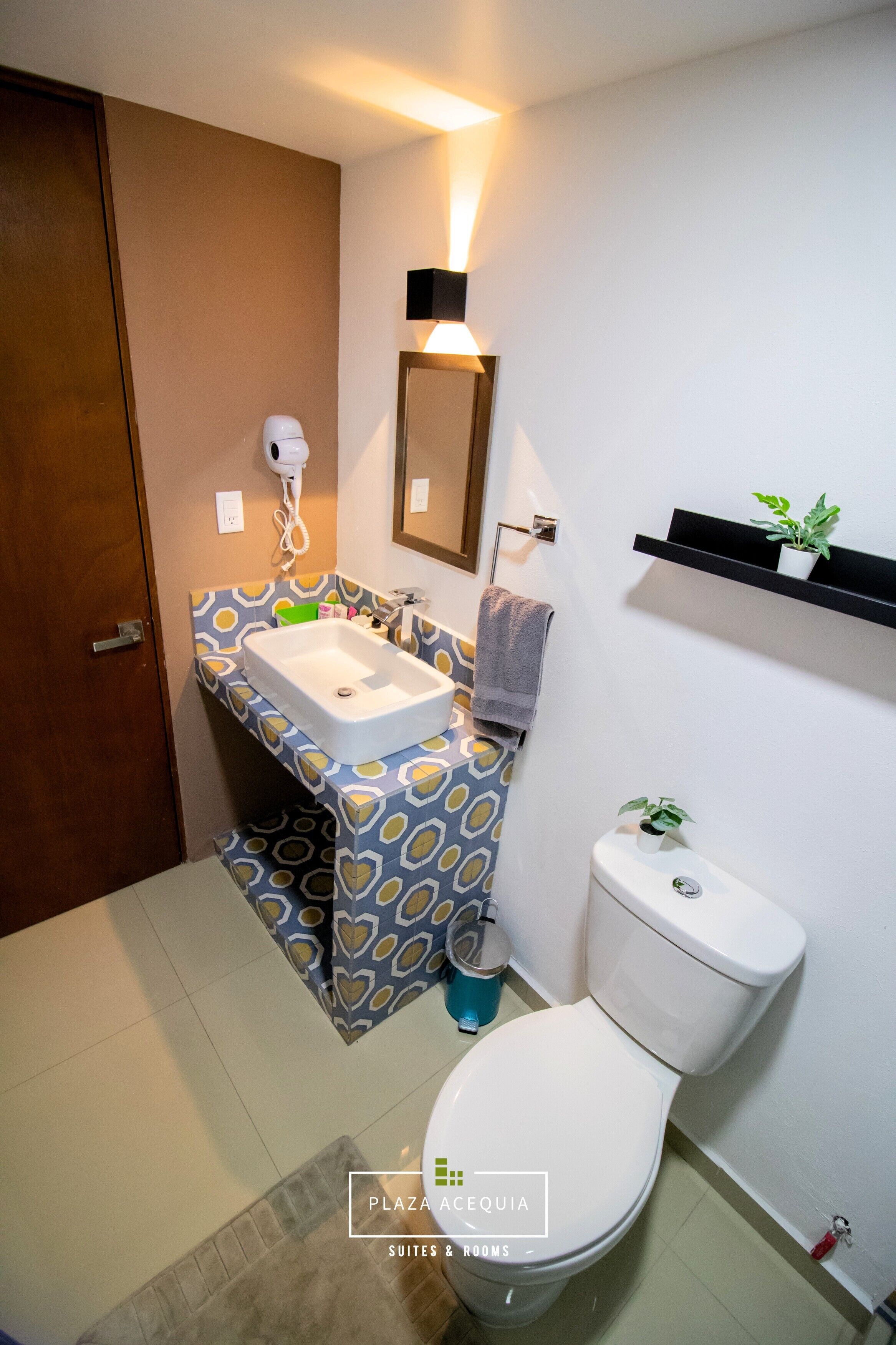 A bathroom with a white sink, a toilet, and a mirror. There is a towel hanging on the wall and a small shelf with plants.