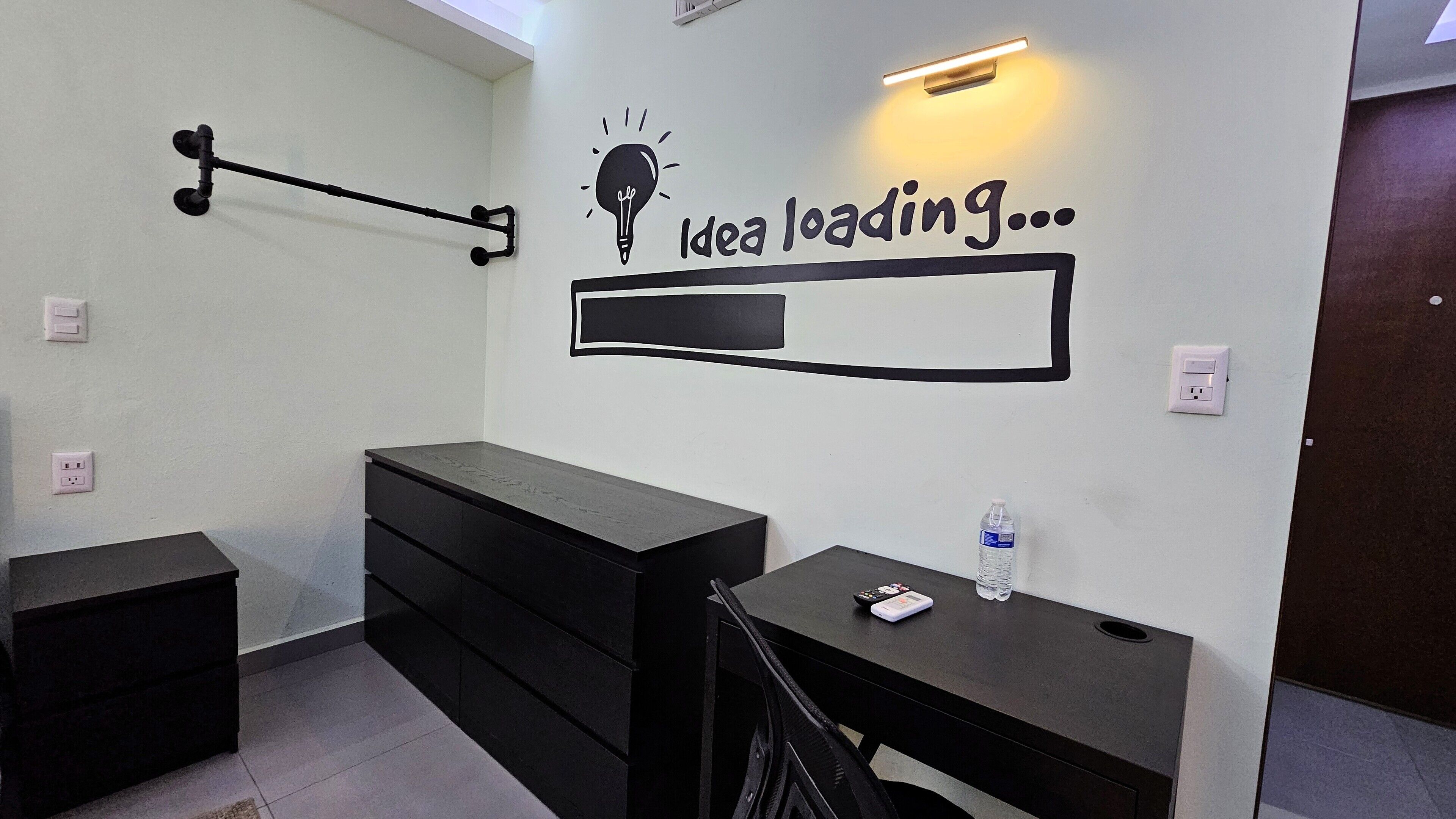 A modern, minimalist room with a desk, a chair, and a wall-mounted light fixture.