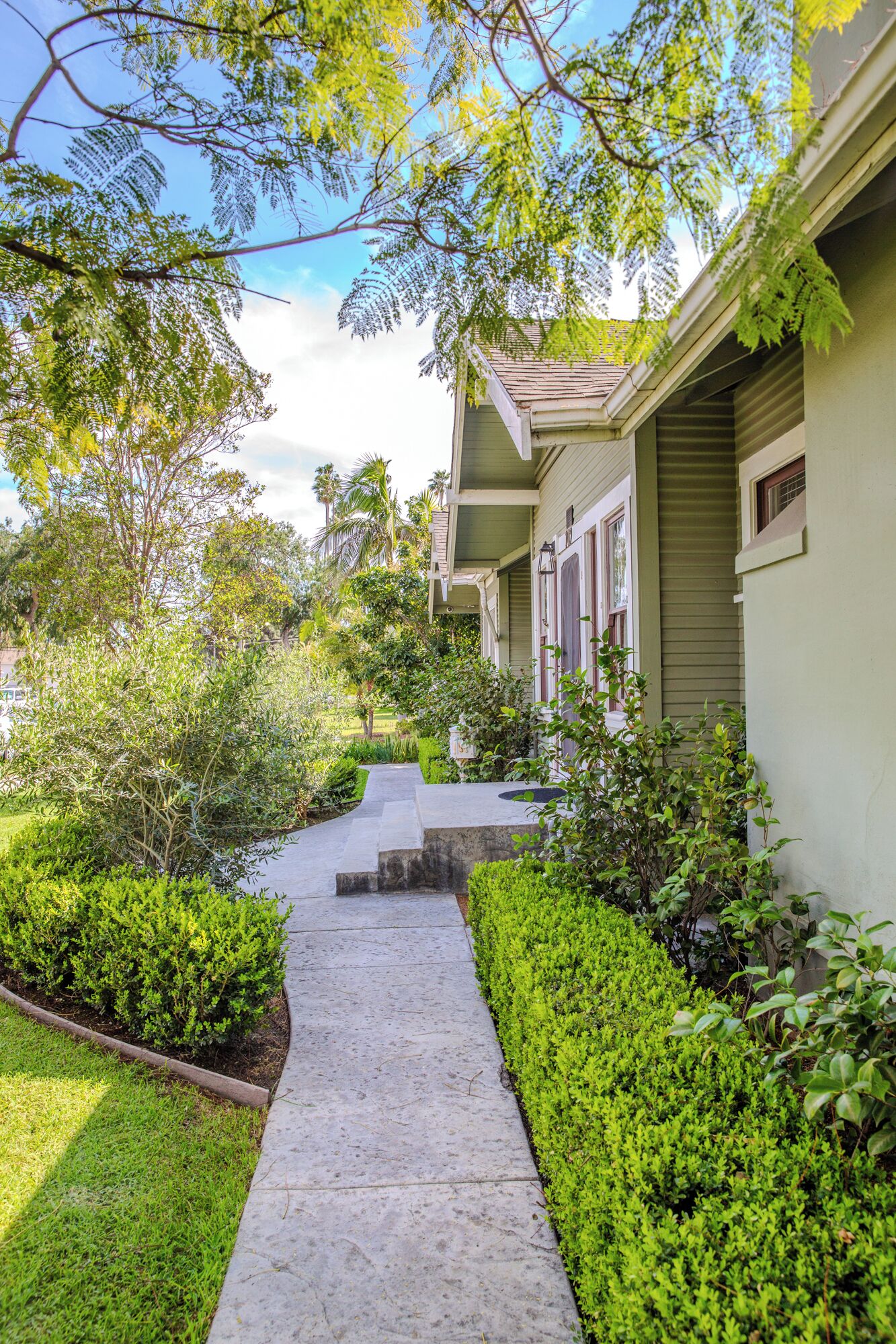 A pathway leading to a house with a porch, surrounded by well-maintained greenery and a clear sky.