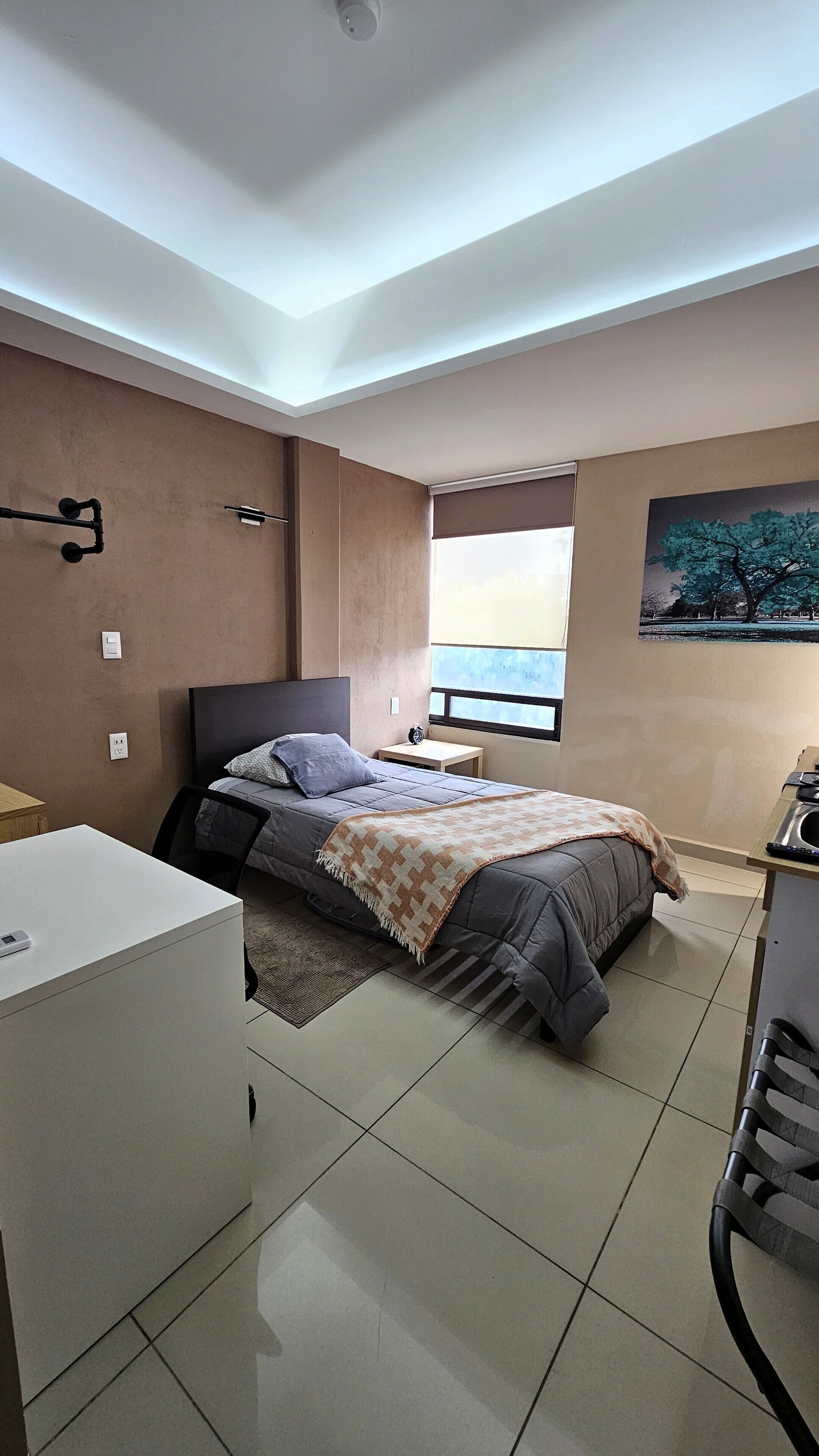 A modern bedroom with a bed, bedside table, and a desk with a chair.