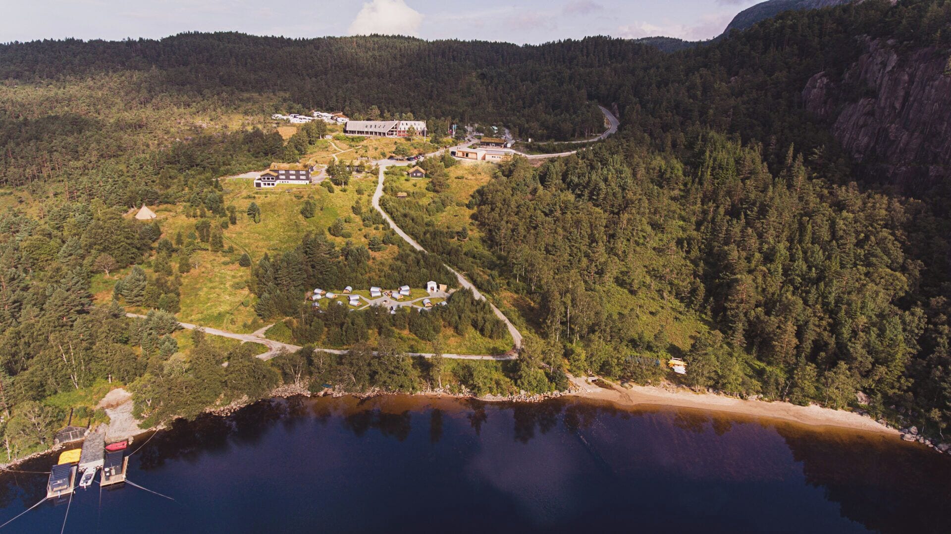 Vista aérea de un complejo turístico junto al lago con cabañas, una casa principal y un muelle.