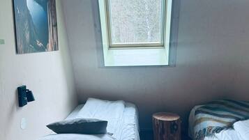 Un dormitorio con dos camas, piso de madera, ventana con vista a árboles y un cuadro en la pared.