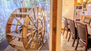 Een rustiek houten waterrad, een eethoek met houten stoelen, en een keuken met houten kasten en een fornuis.