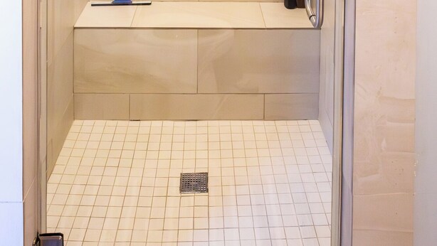 Una ducha a pie con asiento, cabezal de ducha de mano y dispensador de jabón en la pared.