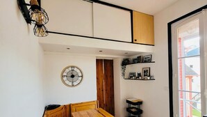 A compact room with a wooden bench and table, a wall clock, and a shelf with framed photos.