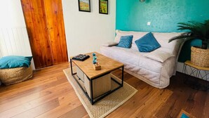 A cozy living room with a wooden floor, a white sofa with blue cushions, a wooden coffee table, and a teal accent wall.