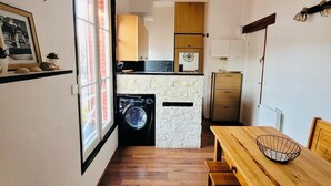 A compact kitchen with a washing machine, wooden dining table, and a small bench.
