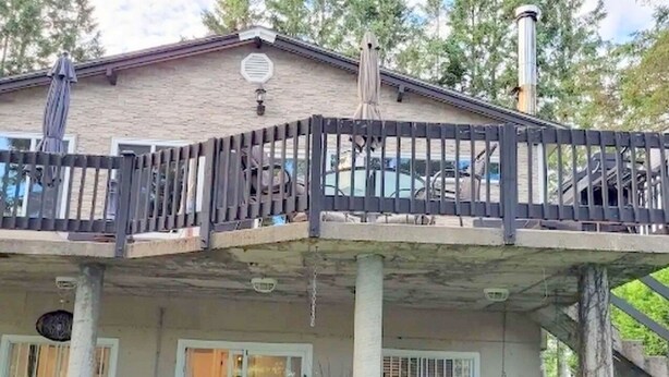 Ein zweistöckiges Haus mit einer überdachten Terrasse und einem umzäunten Deck.