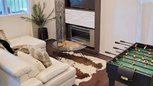 Ein Wohnzimmer mit einer Couch, einem Kicker, einem Kamin und einem Fernseher.