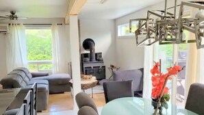 Ein modernes Wohnzimmer mit Esstisch aus Glas, grauen Sofas und einem schwarzen Kamin.
