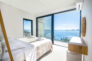 A bedroom with a bed, a nightstand, and a view of the sea.