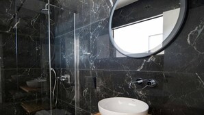 Et moderne badeværelse med en brusekabine i glas, en hvid vask på en træbordplade og et rundt spejl på væggen.
