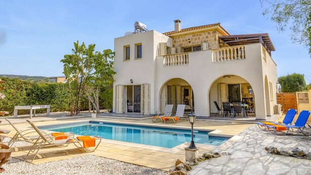 Una casa de dos pisos con piscina, mobiliario exterior y jardín.
