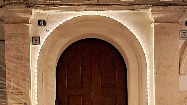 A large, arched doorway with a wooden door, flanked by numbered plaques and a sign indicating 'Palazzo di' on the left.