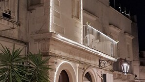 A historic building with a balcony, arched doorways, and a palm tree in front.