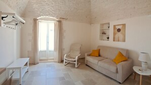 A spacious living area with a high ceiling, a sofa with yellow cushions, a white armchair, a small table, and a lamp.