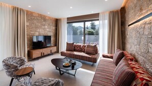 Una sala de estar moderna con una pared de piedra, un televisor de pantalla plana, un sofá, una mesa de centro y un sillón estampado.