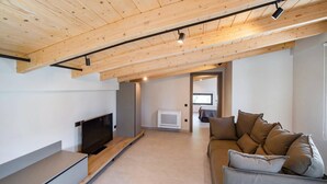 Una sala de estar moderna con techo de madera, un televisor de pantalla plana, un sofá y una pequeña área de cocina con refrigerador y aire acondicionado.